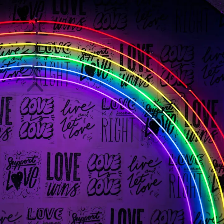 rainbow neon lights over a wall with various pro-LBTQ slogans of love