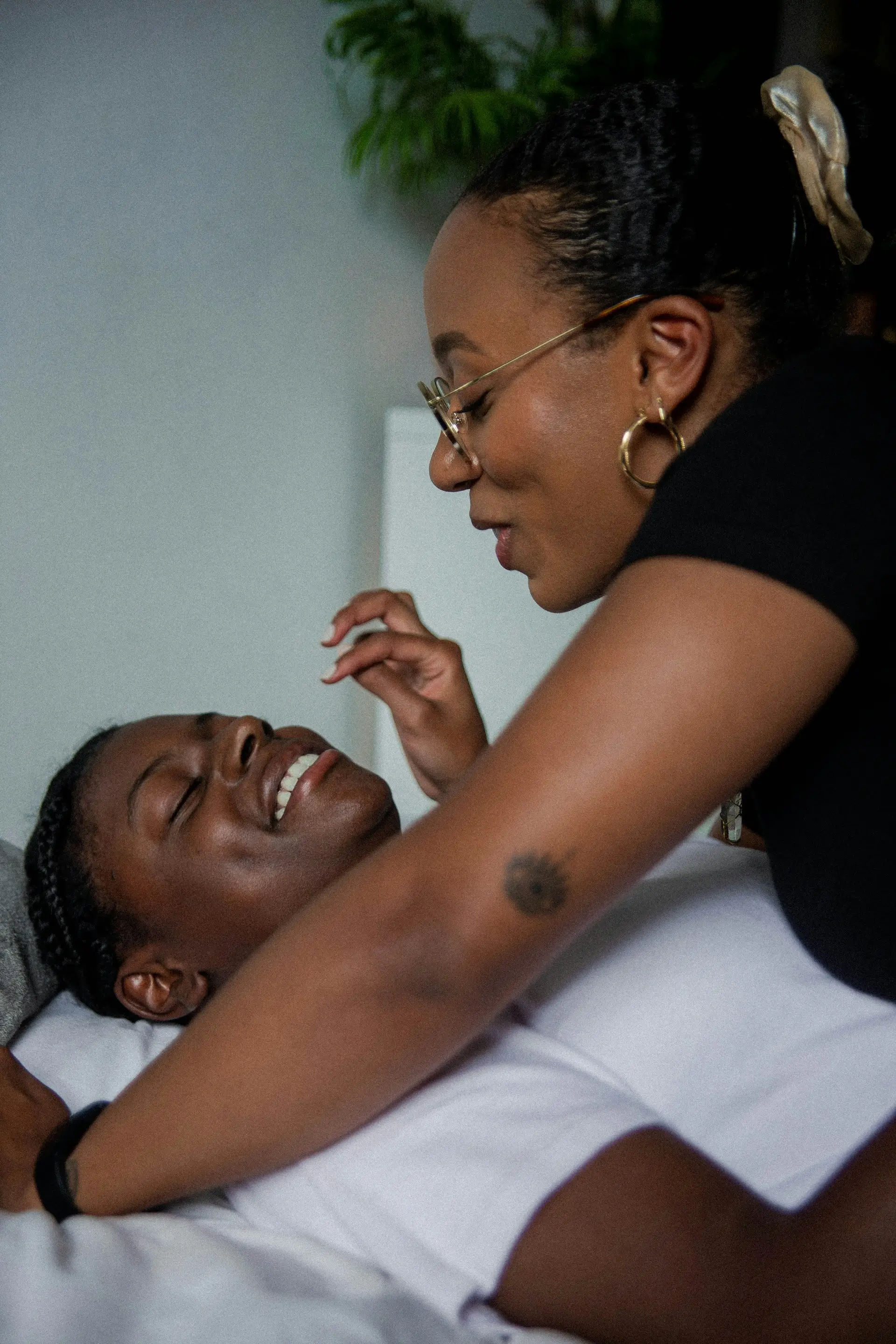 image of two clothed Black people laying in bed on top of each other, smiling at each other